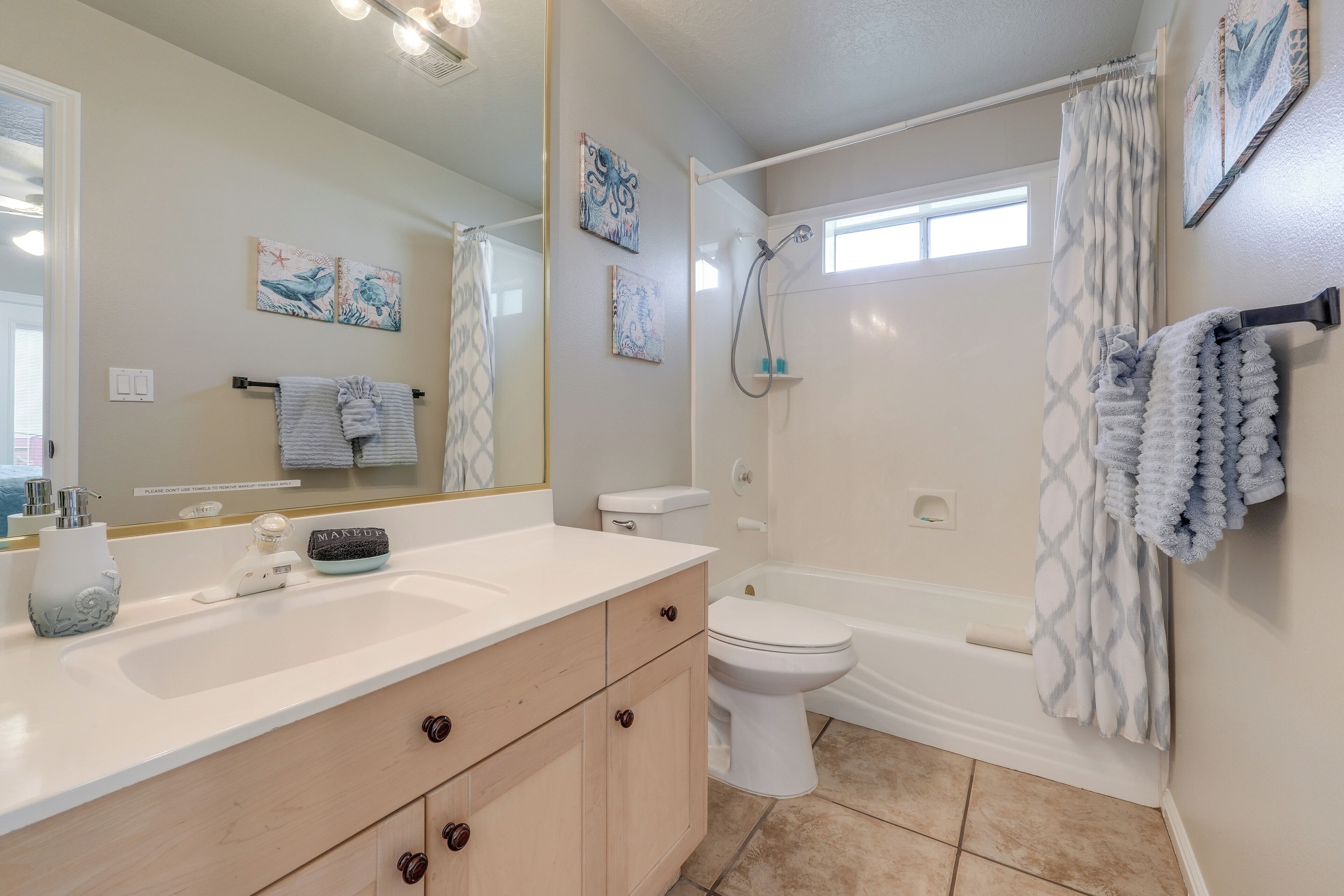 A bathroom with a white sink, vanity, and toilet. There are towels hanging on the wall and a shower curtain.