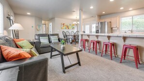 A modern living room with a sofa, coffee table, and red bar stools. There is a kitchen area with a refrigerator and a window. - Family-friendly St George Condo w/ Community Pools (St. George)