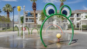 A water play area with circular and arch-shaped structures, a yellow ball, and a building with balconies in the background. - Family-friendly St George Condo w/ Community Pools (St. George)