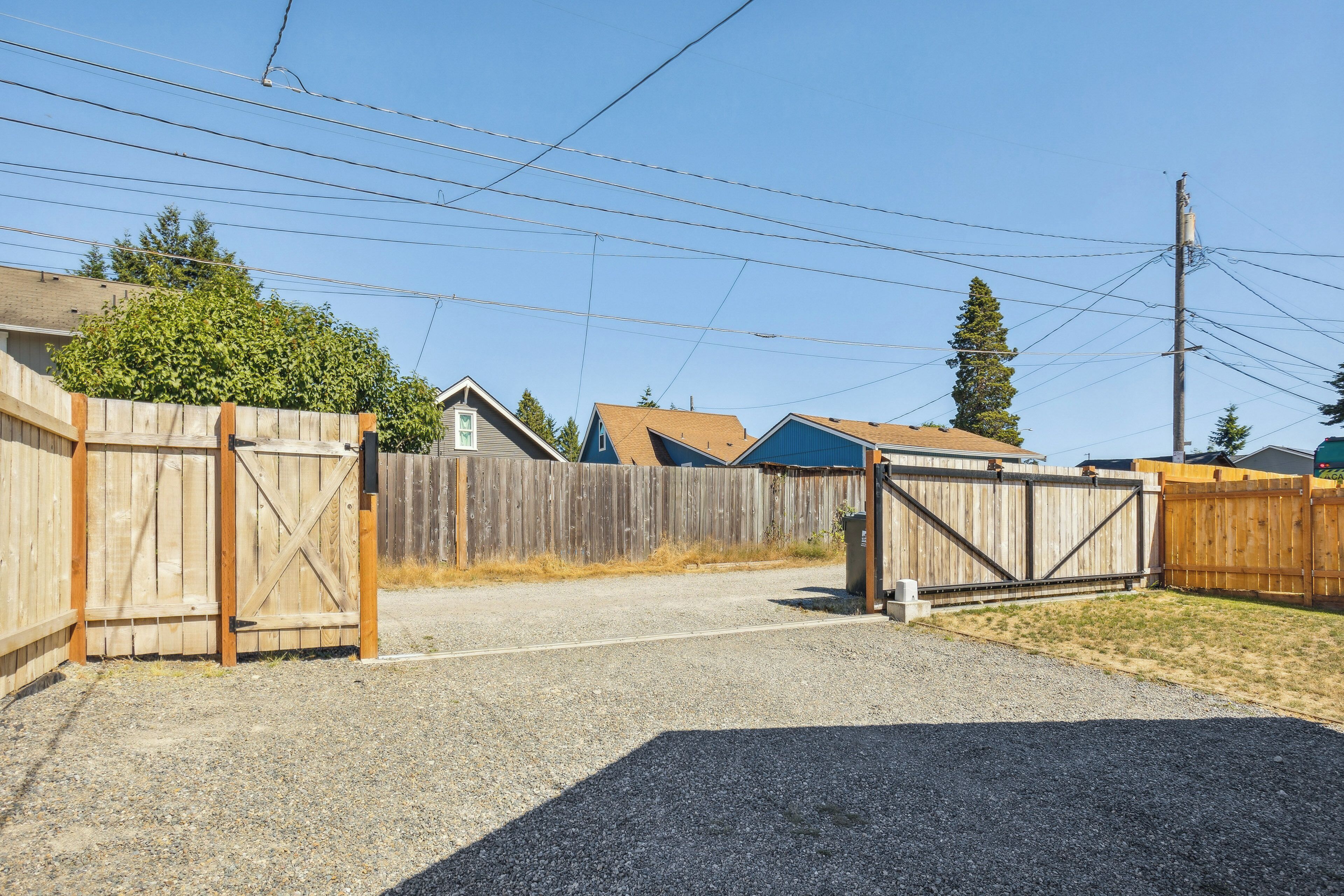 A gated driveway leading to a residential area with houses and a wooden fence.