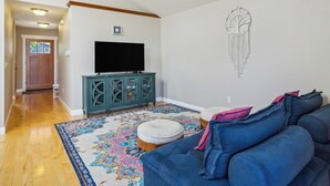 A living room with a blue sofa, a patterned rug, a television on a cabinet, and a dreamcatcher on the wall. - Cheery Tacoma Vacation Rental: 7 Mi to Owen Beach! (Tacoma)