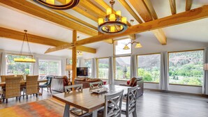 A spacious living area with a wooden dining table, comfortable seating, and large windows offering a view of the outdoors. - Stunning Ouray Escape w/ Panoramic Mountain Views! (Ouray)