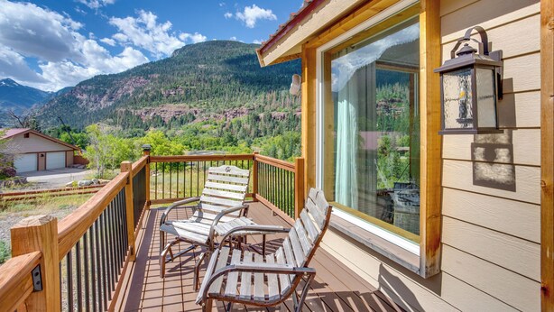 A wooden deck with two chairs and a large window overlooking a mountainous landscape. - Stunning Ouray Escape w/ Panoramic Mountain Views! (Ouray)