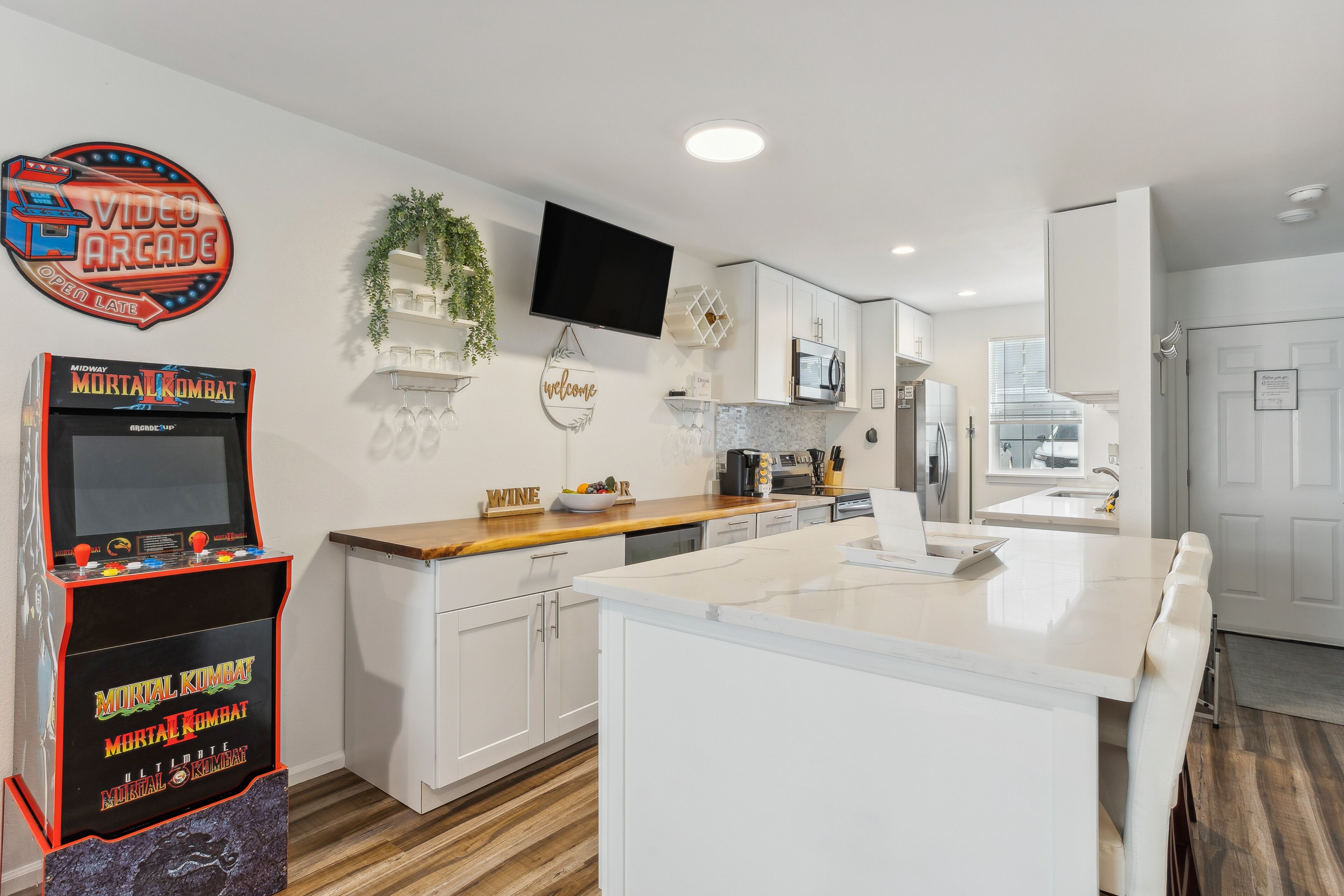 A modern kitchen with white cabinetry, a wooden countertop, a built-in oven, and a flat-screen TV mounted above the counter.