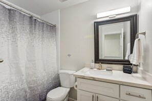 A bathroom with a white toilet, a sink with a marble countertop, a dark-framed mirror, and a shower curtain with a geometric pattern. - Charming Tacoma Retreat w/ Patio & 2 Fireplaces! (Tacoma)