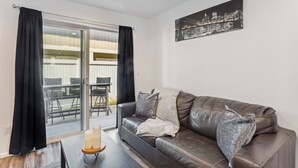 A modern living room with a leather sofa, a glass door leading to an outdoor area, and a cityscape artwork on the wall. - Charming Tacoma Retreat w/ Patio & 2 Fireplaces! (Tacoma)