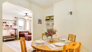 A dining area with a wooden table set for four, surrounded by wooden chairs. There is a vase with flowers on the table, and a shelf with boxes and kitchen items in the background. - Cottage w/ Furnished Deck: 1 Mi to Dtwn Craig! (Craig)