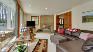 A spacious living room with a stone fireplace, leather sofas, and a large window overlooking a forest. - Mendon Home w/ Hot Tub, Fire Pit & Near Skiing! (Rutland)