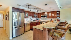 A spacious kitchen with stainless steel appliances, wooden cabinets, and a large island with bar stools. - Beachfront St Augustine Beach Condo, Stunning View (St. Augustine)