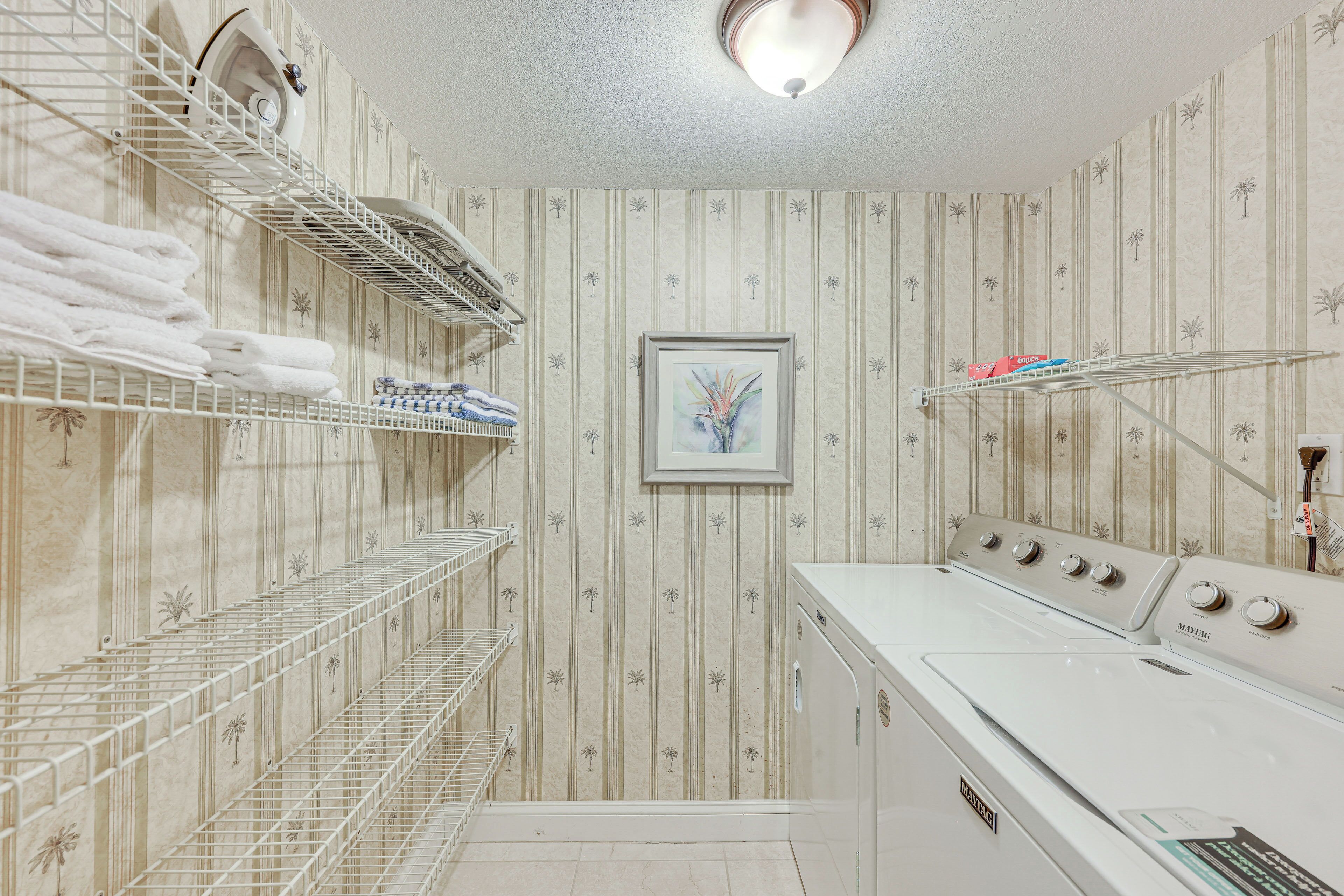 A laundry room with a white washing machine, shelves with folded towels, and a framed picture on the wall.