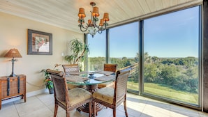 A dining area with a glass table, wicker chairs, and a chandelier. - Beachfront St Augustine Beach Condo, Stunning View (St. Augustine)