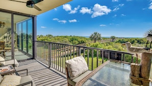 A balcony with a glass door, a ceiling fan, and a view of the ocean and greenery. - Beachfront St Augustine Beach Condo, Stunning View (St. Augustine)
