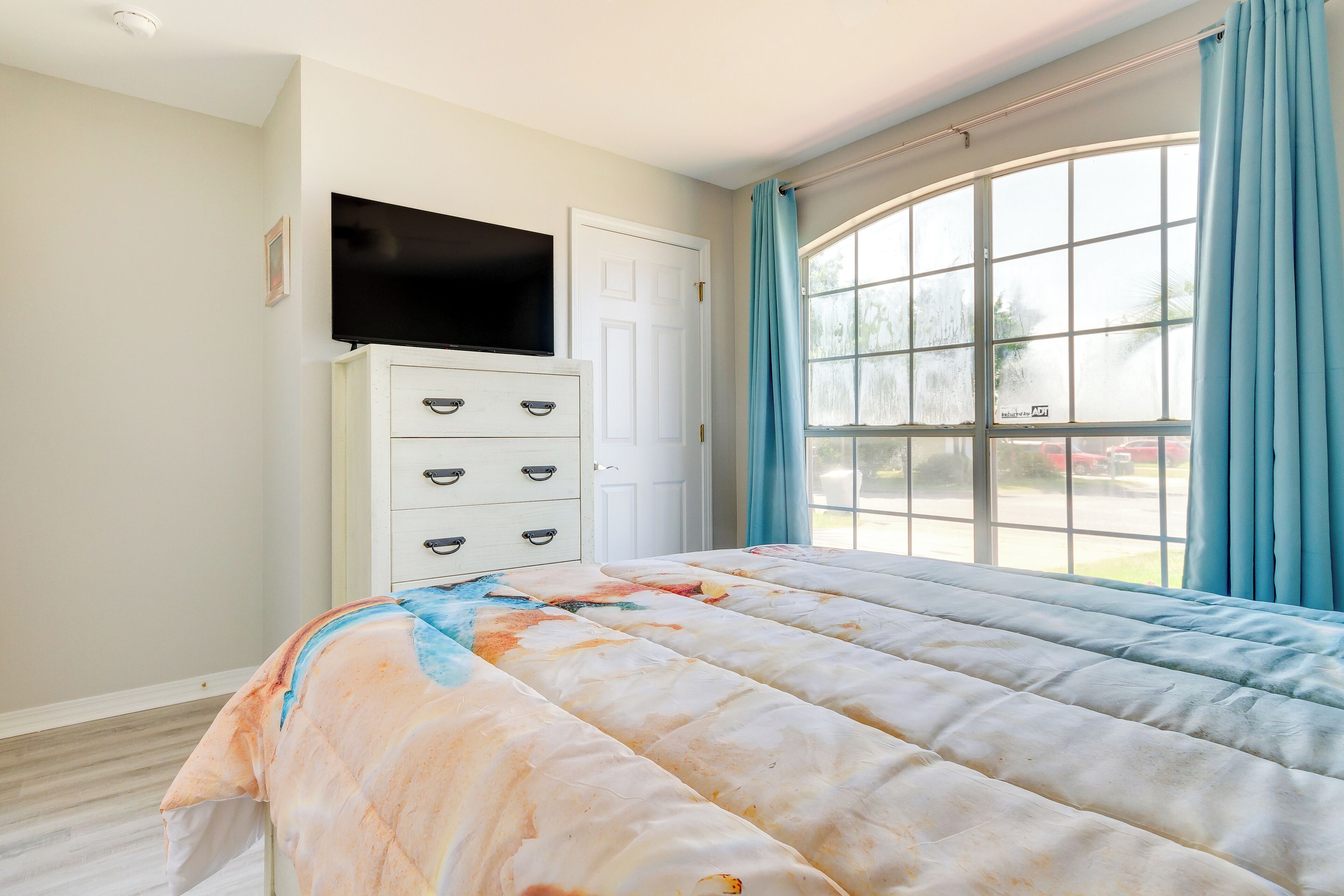 A bedroom with a bed, a dresser, a television, and a large window with curtains.