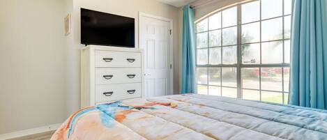 A bedroom with a bed, a dresser, a television, and a large window with curtains.