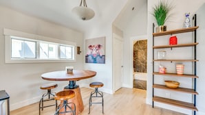 A modern kitchen with a round wooden table, bar stools, a hanging light fixture, and a decorative shelf with various items. - 14 Mi to Dtwn Denver: Sleek Westminster Home (Westminster)