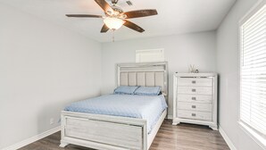 Een slaapkamer met een bed, een kaptafel en een plafondventilator.