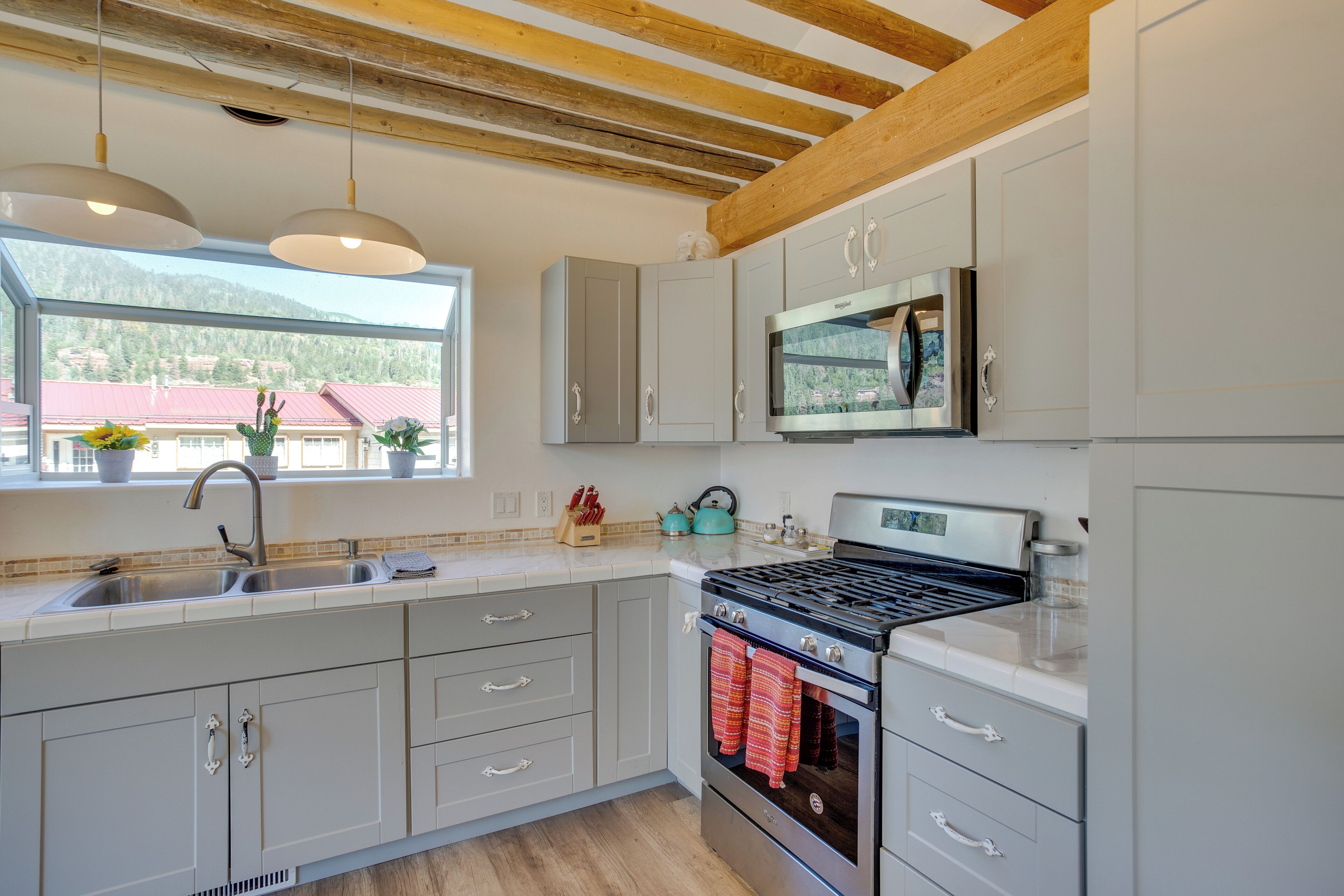 Une cuisine moderne avec des meubles gris, une cuisinière en acier inoxydable et une fenêtre donnant sur des immeubles.