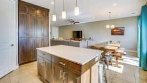 A modern kitchen with wooden cabinets, a large island, pendant lights, and a dining area with a table and chairs. - Moab Vacation Rental: Pool & Hot Tub Access! (Moab)