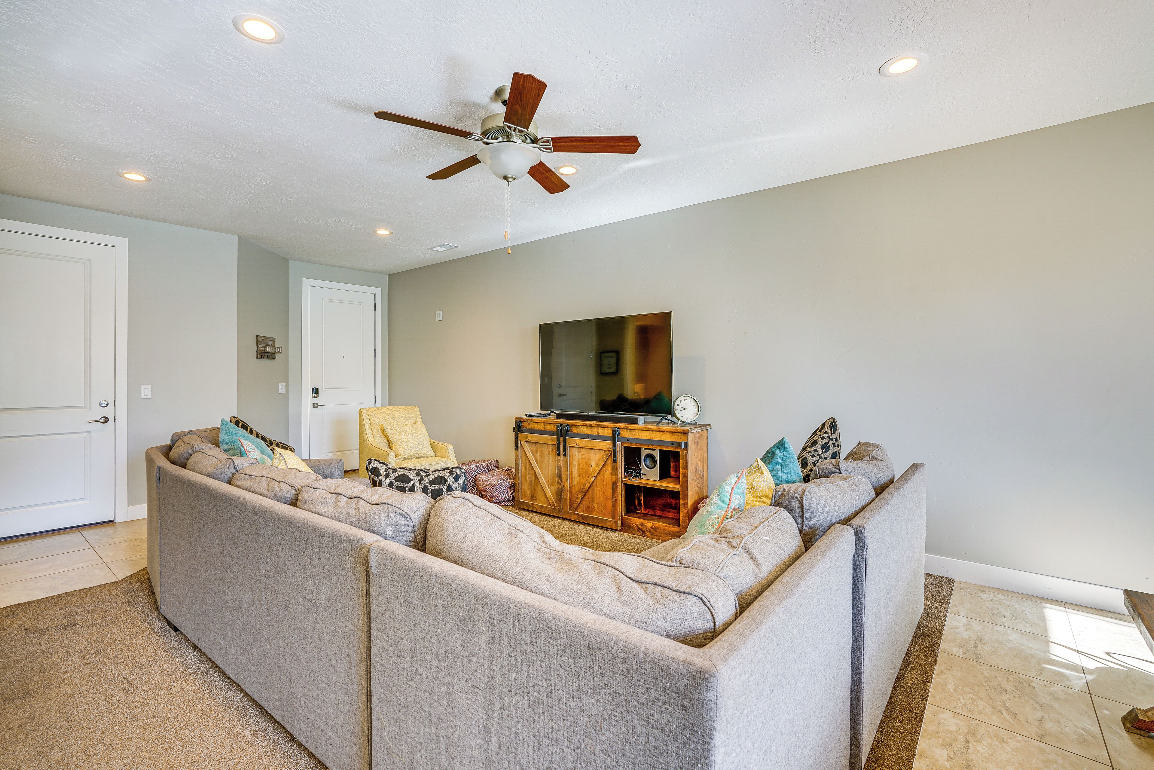 A living room with a large sectional sofa, a wooden cabinet, and a ceiling fan.