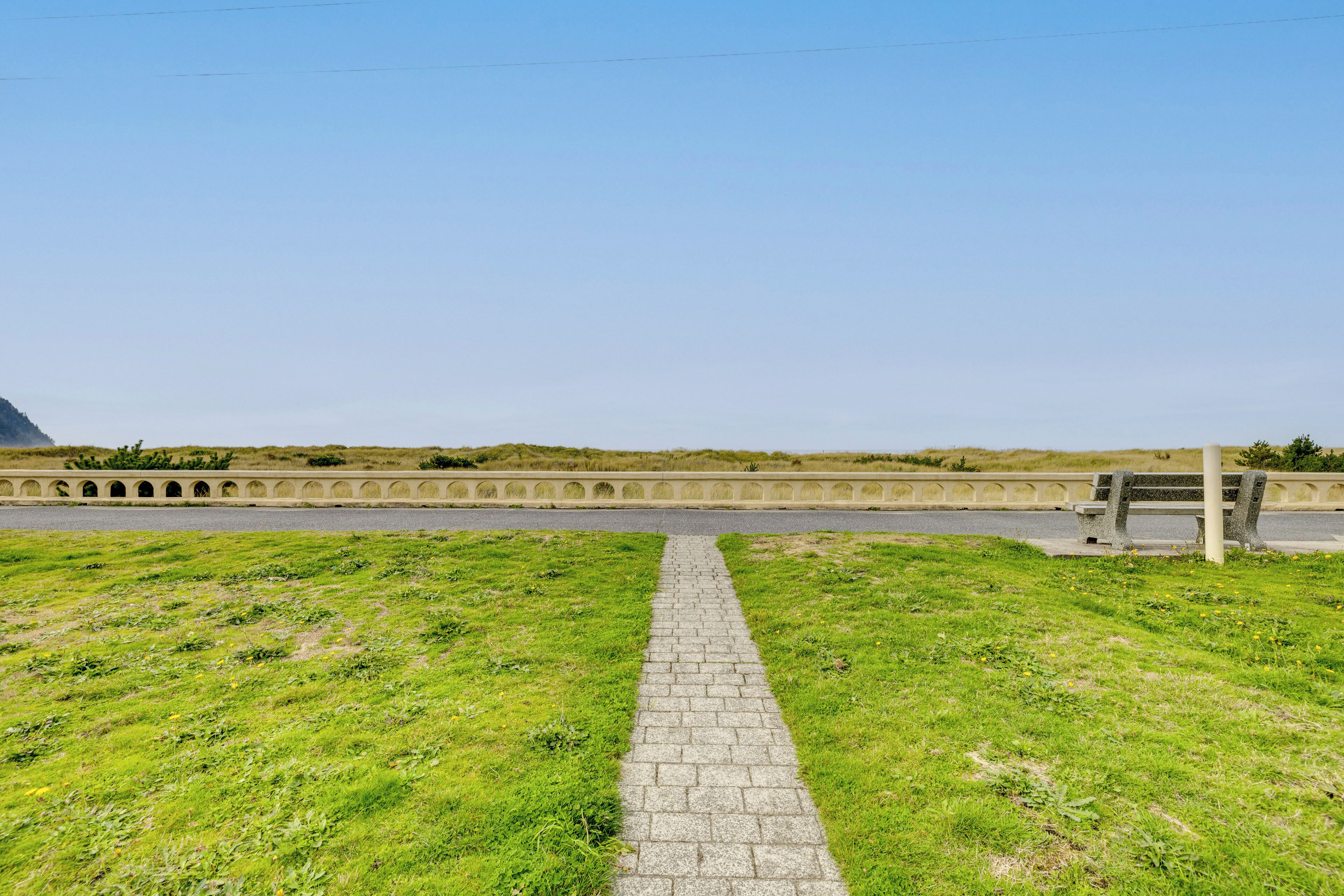 Een verhard pad dat leidt naar een brug over een waterpartij, met een grasveld aan beide zijden en een heldere lucht erboven.