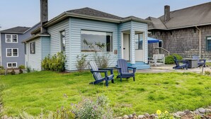 A light blue house with a small deck and two Adirondack chairs. - Beachfront Cottage on Seaside Promenade w/ Hot Tub (Seaside)