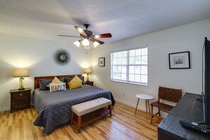 A bedroom with a bed, a bench, a desk, a chair, a TV, and a ceiling fan.