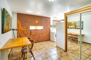 Un comedor con mesa y sillas de madera, un mural en la pared y piso de baldosas.