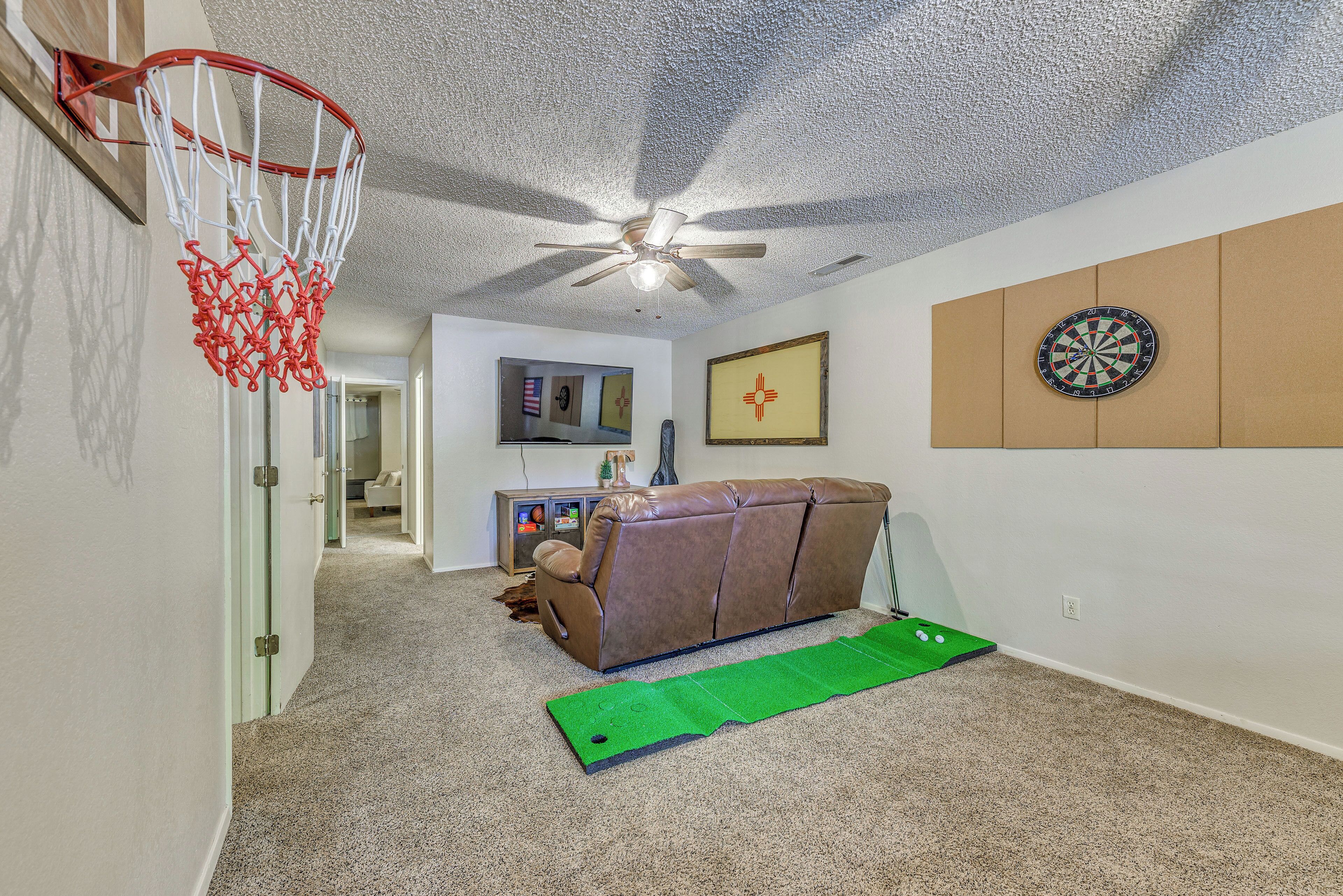 Um interior de casa com um cesto de basquete, um ventilador de teto, um sofá, um alvo de dardos e um tapete verde no chão.