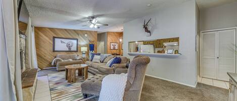 A living room with a sofa, armchair, ottoman, and a ceiling fan.