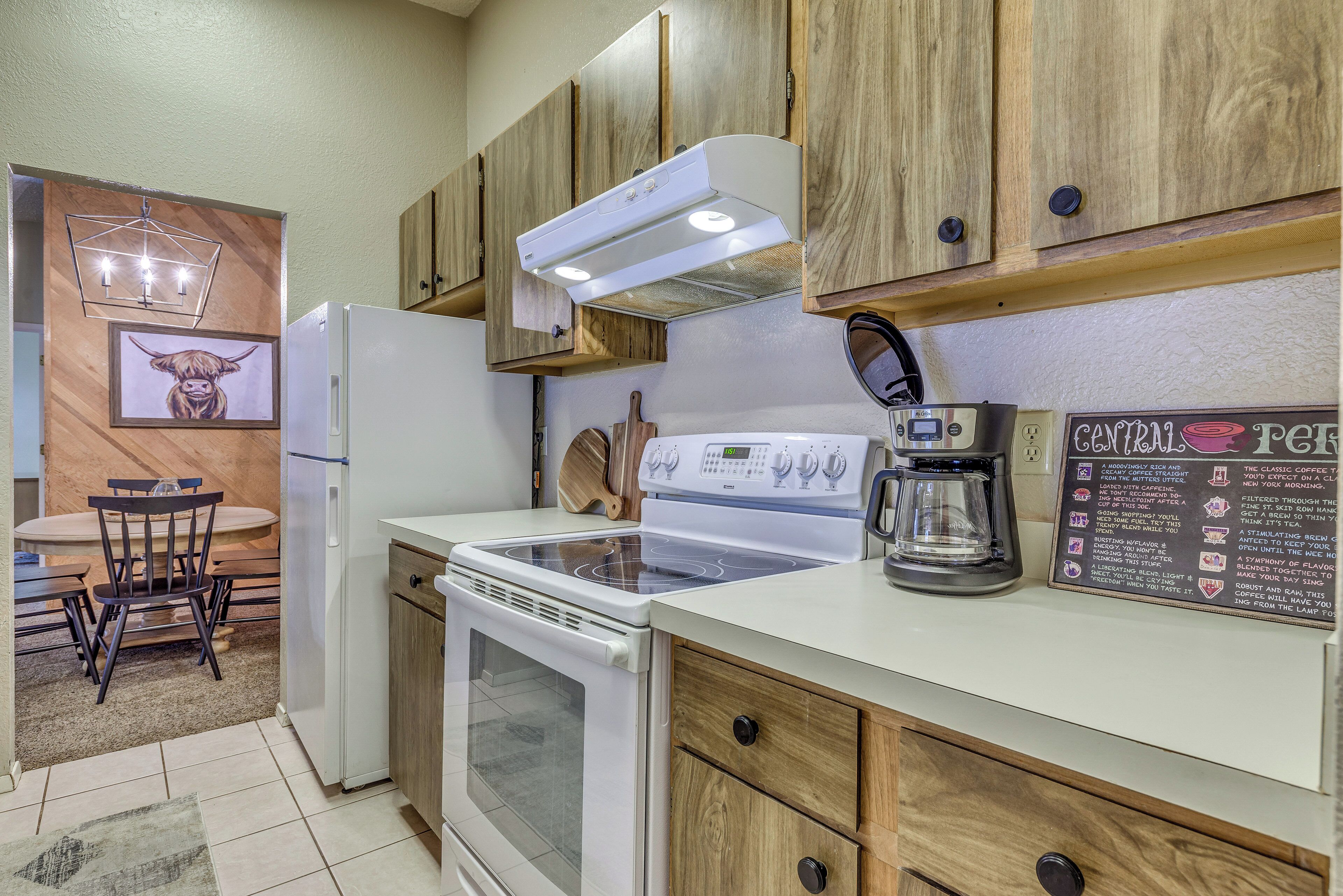 A compact kitchen with wooden cabinets, a built-in oven, a coffee maker, and a chalkboard menu.