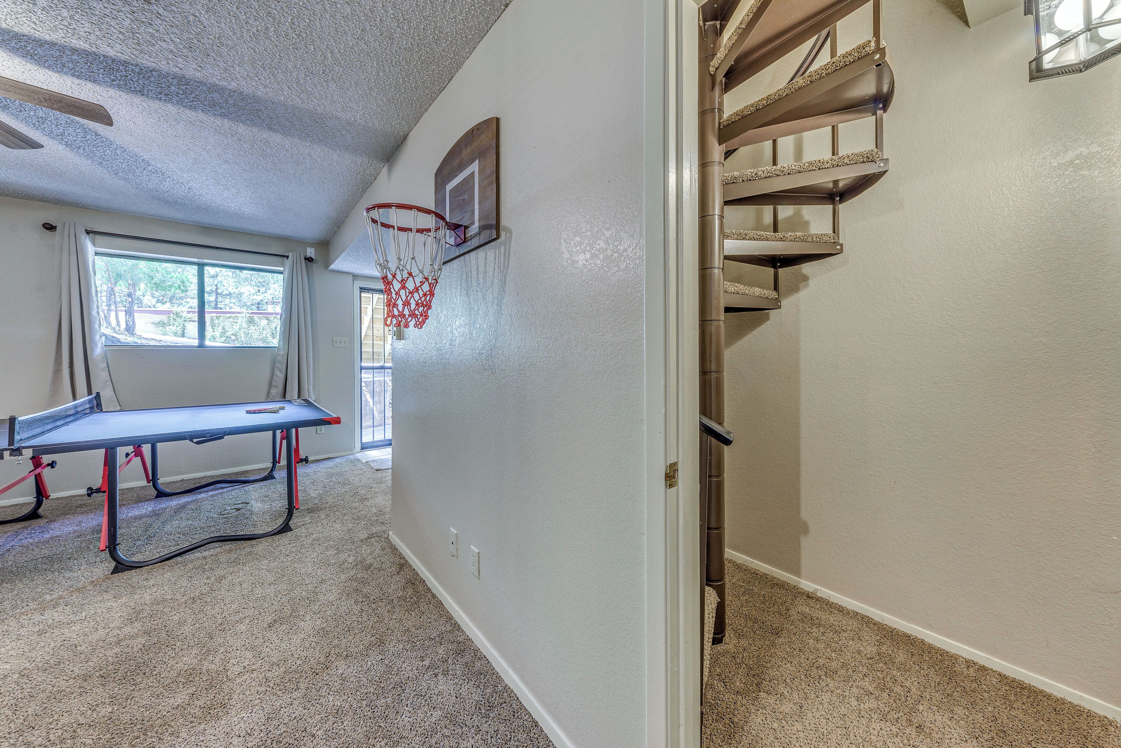 A hallway with a ping pong table, a basketball hoop, and a staircase.