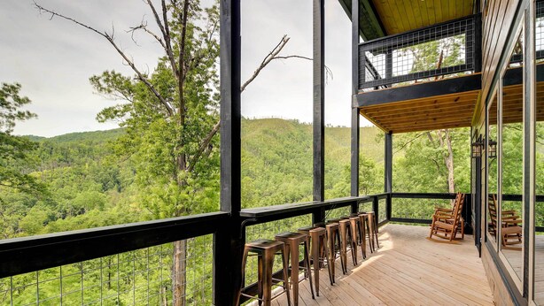 A wooden deck with bar stools and chairs overlooking a forested hillside. - Cobbly Nob Resort Cabin: Hot Tub, Pool & Views! (Gatlinburg)