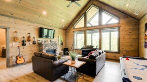 A cozy living room with a fireplace, wooden walls, a pool table, and a large window. - Cobbly Nob Resort Cabin: Hot Tub, Pool & Views! (Gatlinburg)