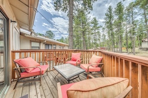 A wooden deck with wicker furniture and a table, surrounded by tall pine trees.