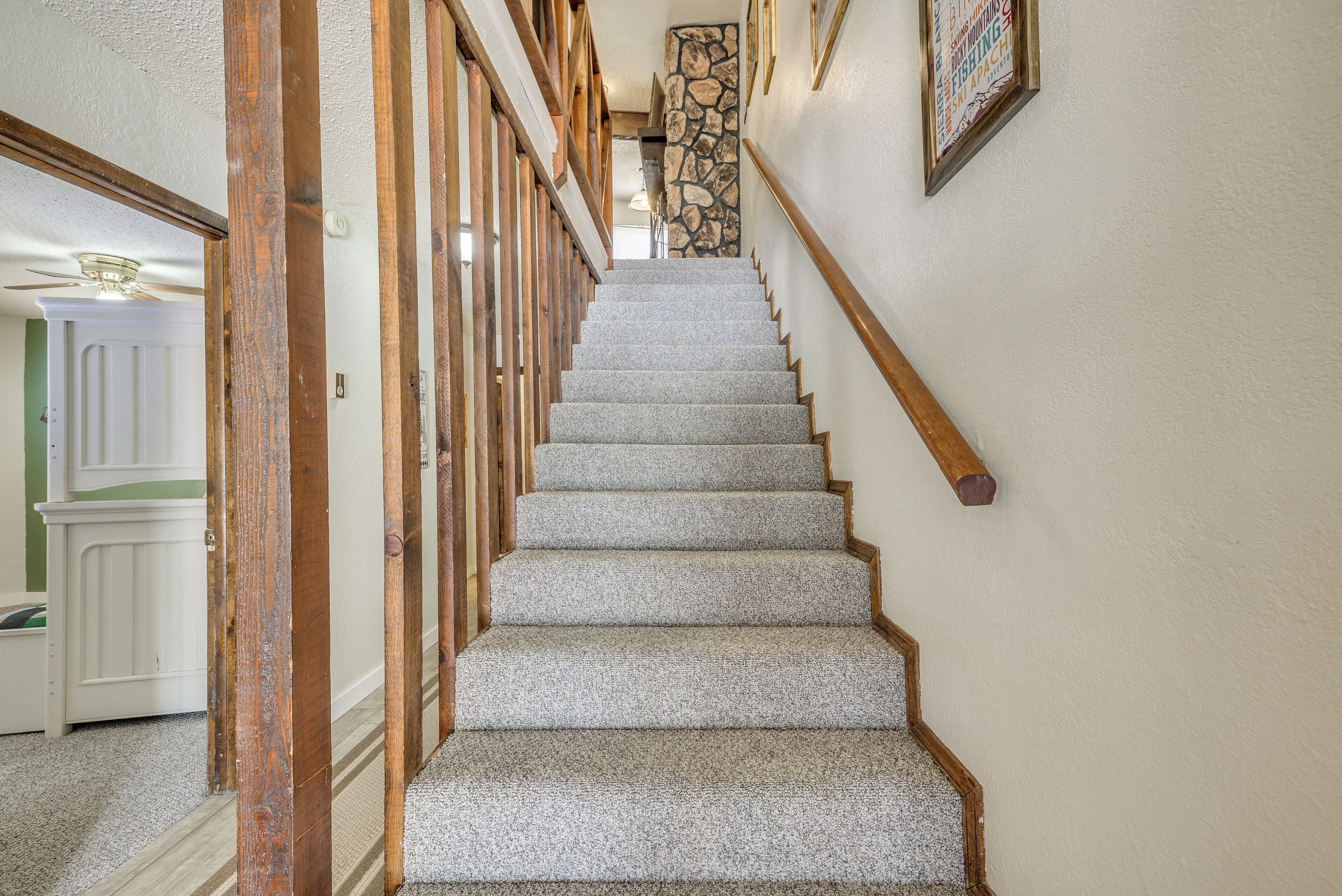 Un escalier avec des rampes en bois et des marches recouvertes de moquette, menant à une pièce dont un mur est habillé de pierres apparentes.