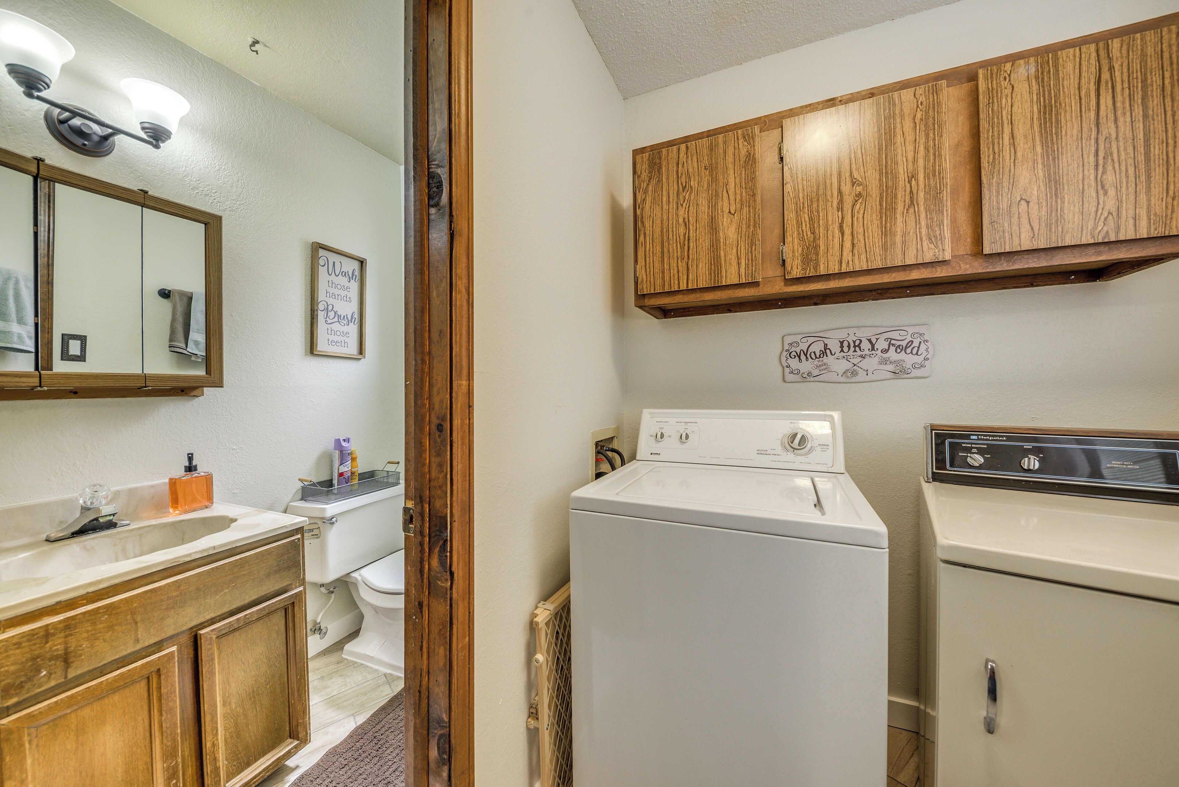 A bathroom with a wooden vanity, a sink, a mirror, a toilet, and a washing machine.