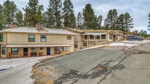 A row of single-story buildings with a covered porch area, likely a motel or small hotel, surrounded by pine trees. - Ruidoso Home w/ Balcony ~ 16 Mi to Ski Apache! (Ruidoso)