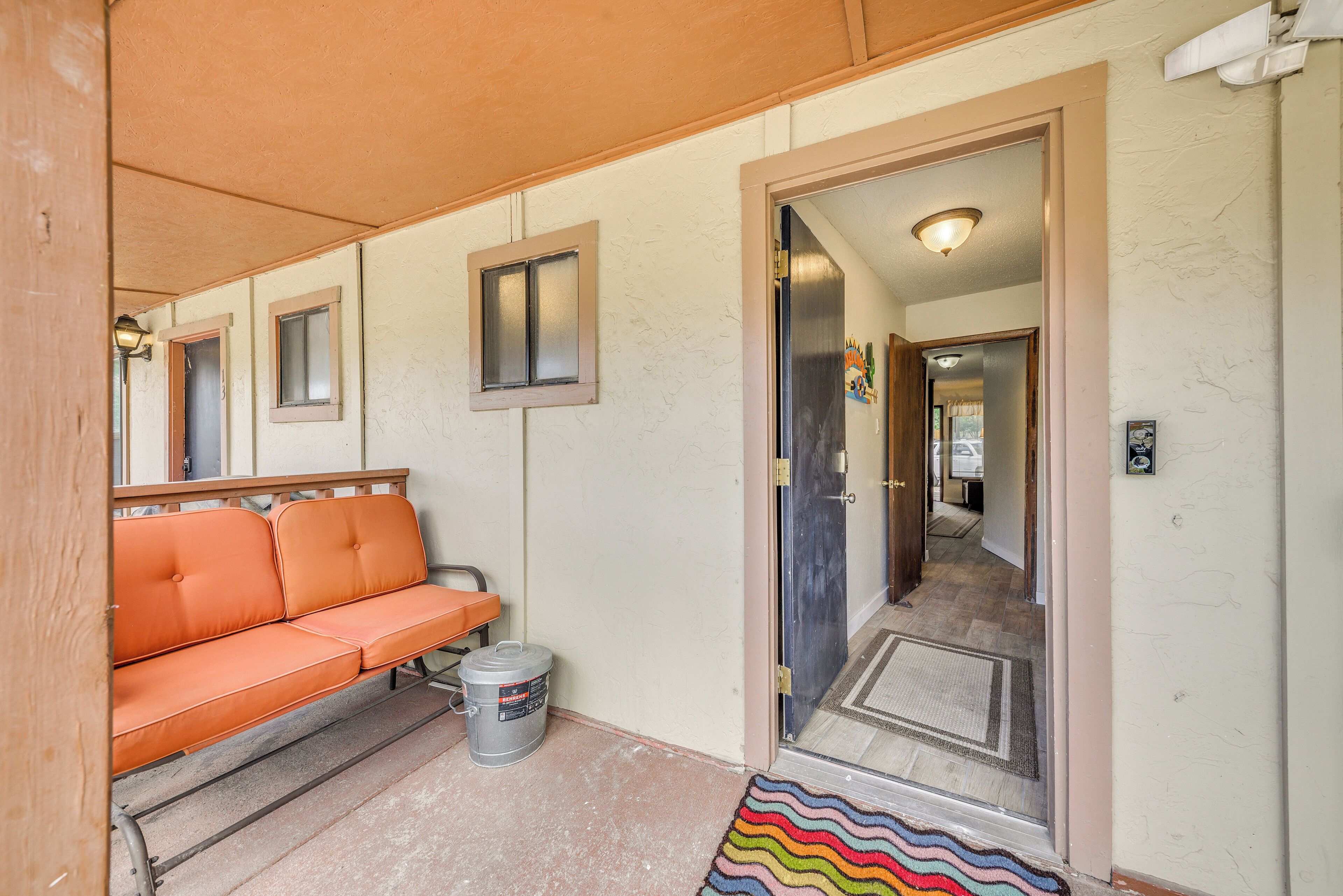 A hallway with a wooden bench, a door, and a small trash can.
