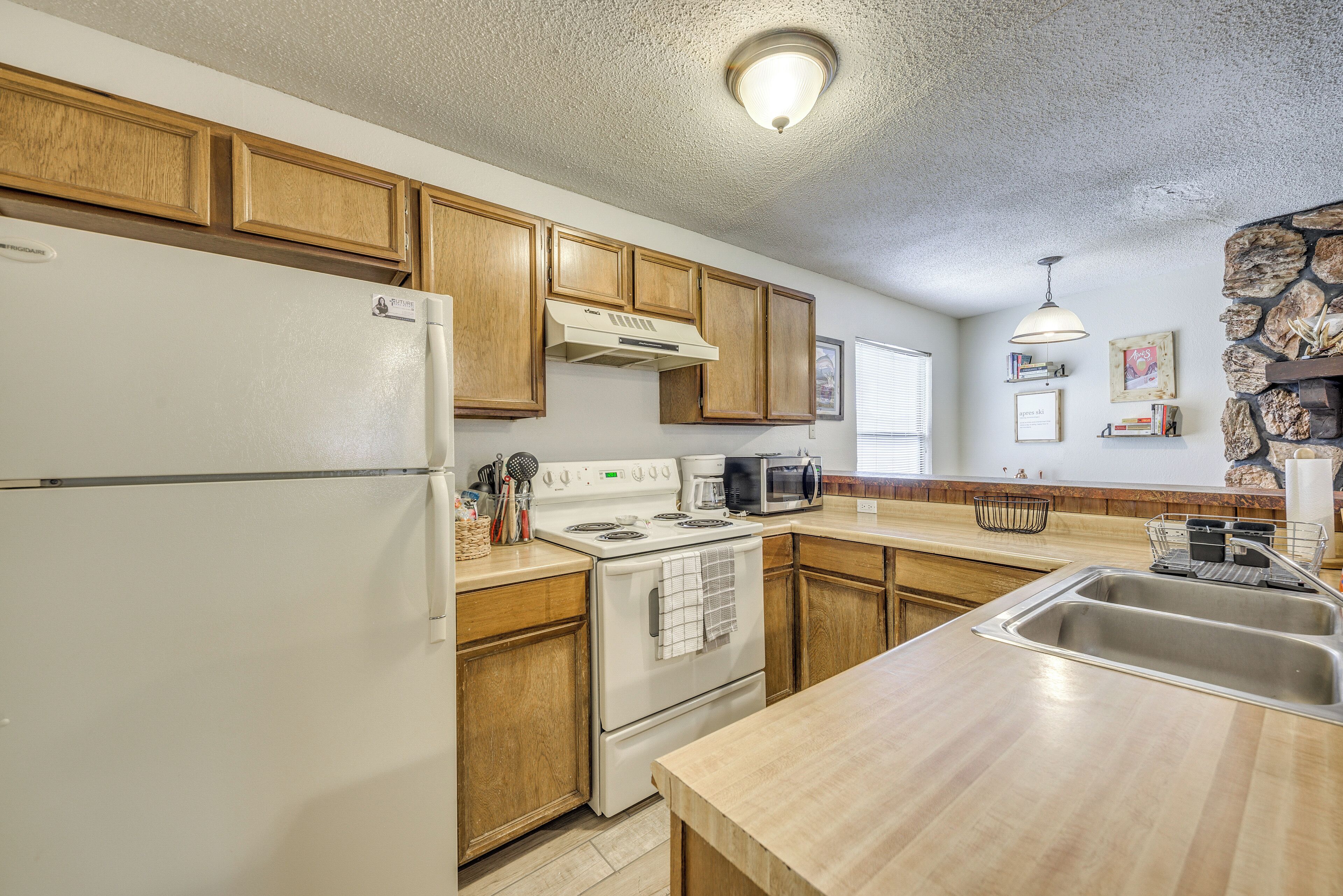 A kitchen with wooden cabinets, a white refrigerator, a stove, a microwave, and a sink.