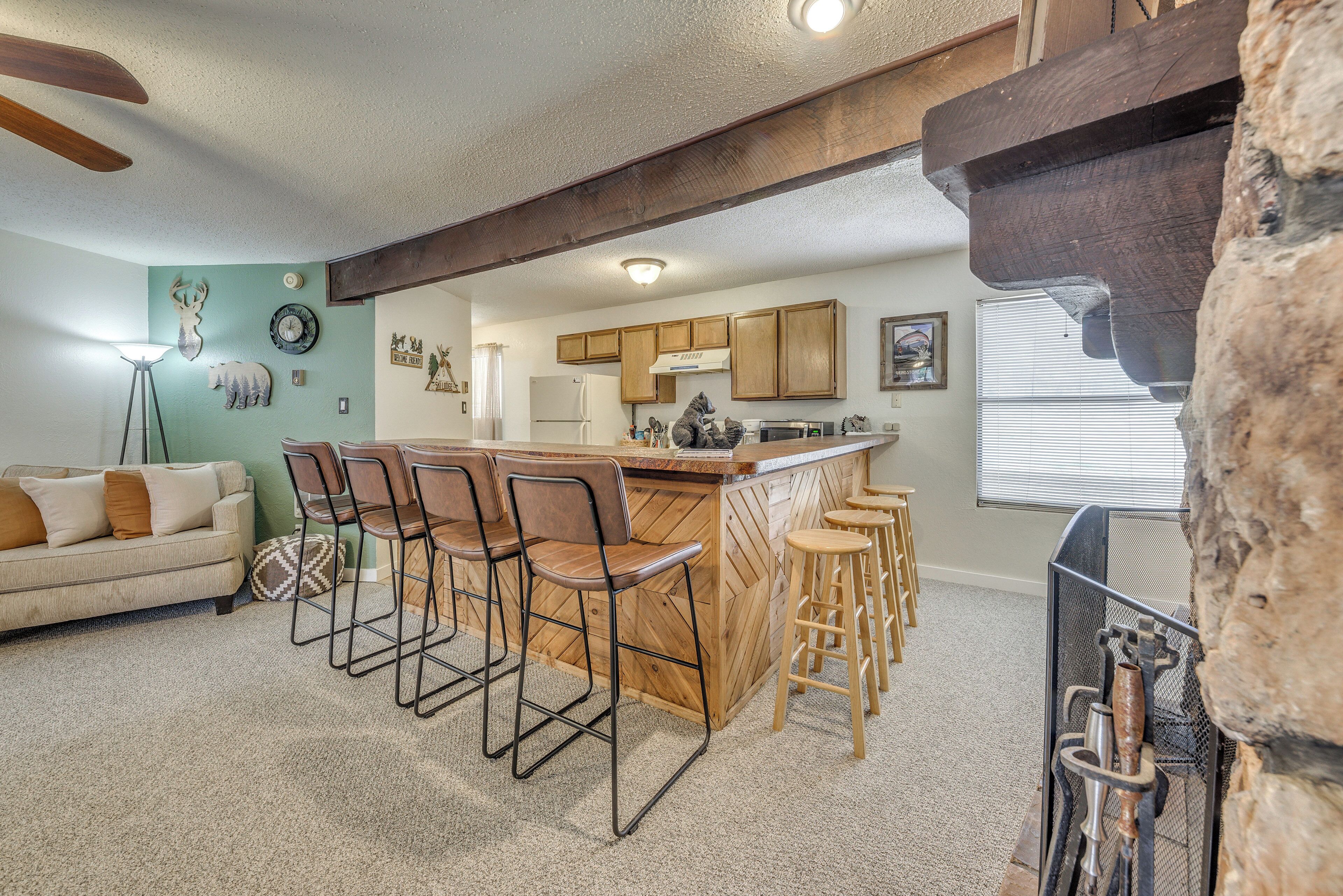 A kitchen with wooden cabinets, a bar area with stools, a refrigerator, and a stone wall.