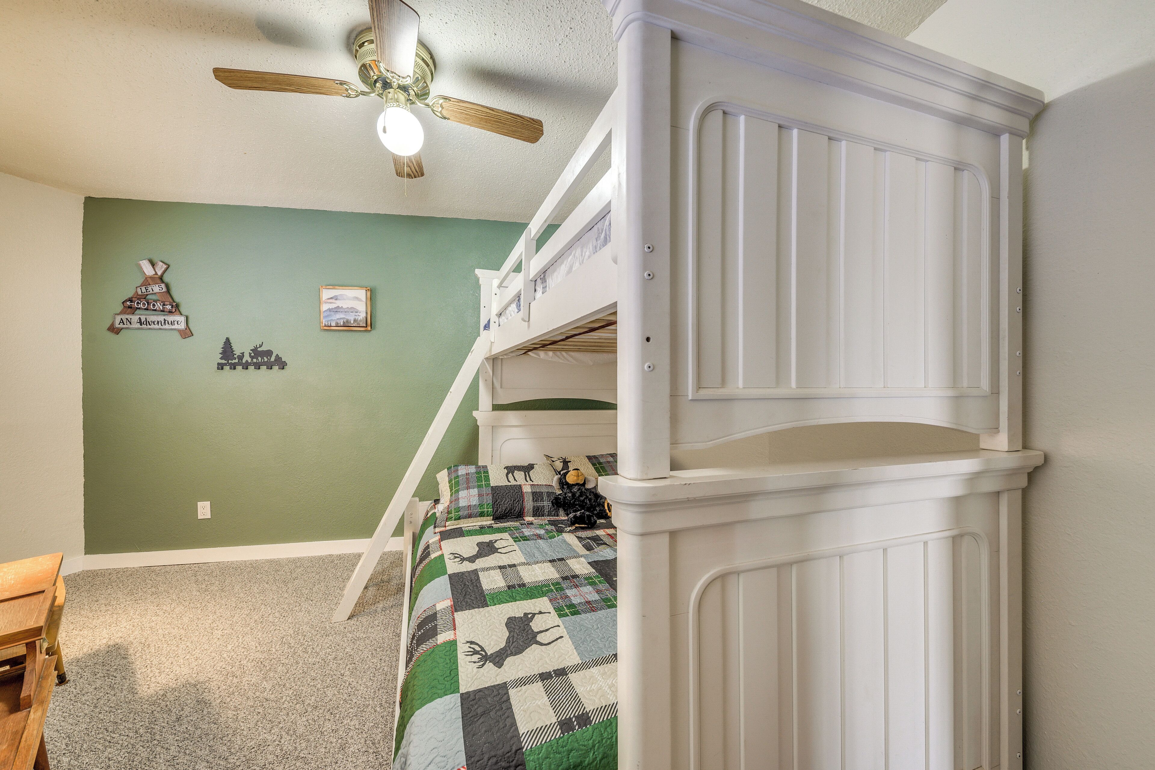 A bunk bed room with a ceiling fan, a green wall, and a checkered bedspread.