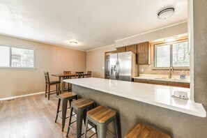 A modern kitchen with a large island, bar stools, wooden cabinets, and a stainless steel refrigerator. - Serene Ruidoso Cabin w/ Fenced Yard Near Downtown! (Ruidoso)