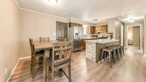 A modern kitchen with a central island, wooden dining table, and bar stools. - Serene Ruidoso Cabin w/ Fenced Yard Near Downtown! (Ruidoso)