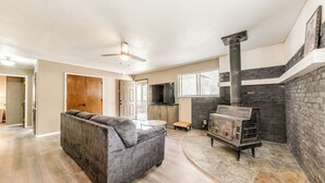 A modern living room with a gray sofa, a stone fireplace, and a television in the background. - Serene Ruidoso Cabin w/ Fenced Yard Near Downtown! (Ruidoso)