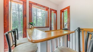 A dining area with a wooden table and chairs, large windows with a forest view, and a small plant on the table. - Inn of the Mountain Goats Ruidoso Cabin w/ Deck! (Ruidoso)