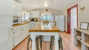 A kitchen with white cabinets, a wooden countertop, and a central island with stools. - Inn of the Mountain Goats Ruidoso Cabin w/ Deck! (Ruidoso)