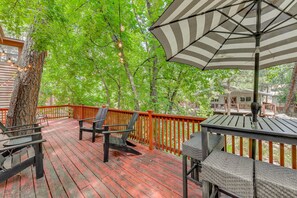 A wooden deck with outdoor furniture, a striped umbrella, and a view of trees. - Inn of the Mountain Goats Ruidoso Cabin w/ Deck! (Ruidoso)