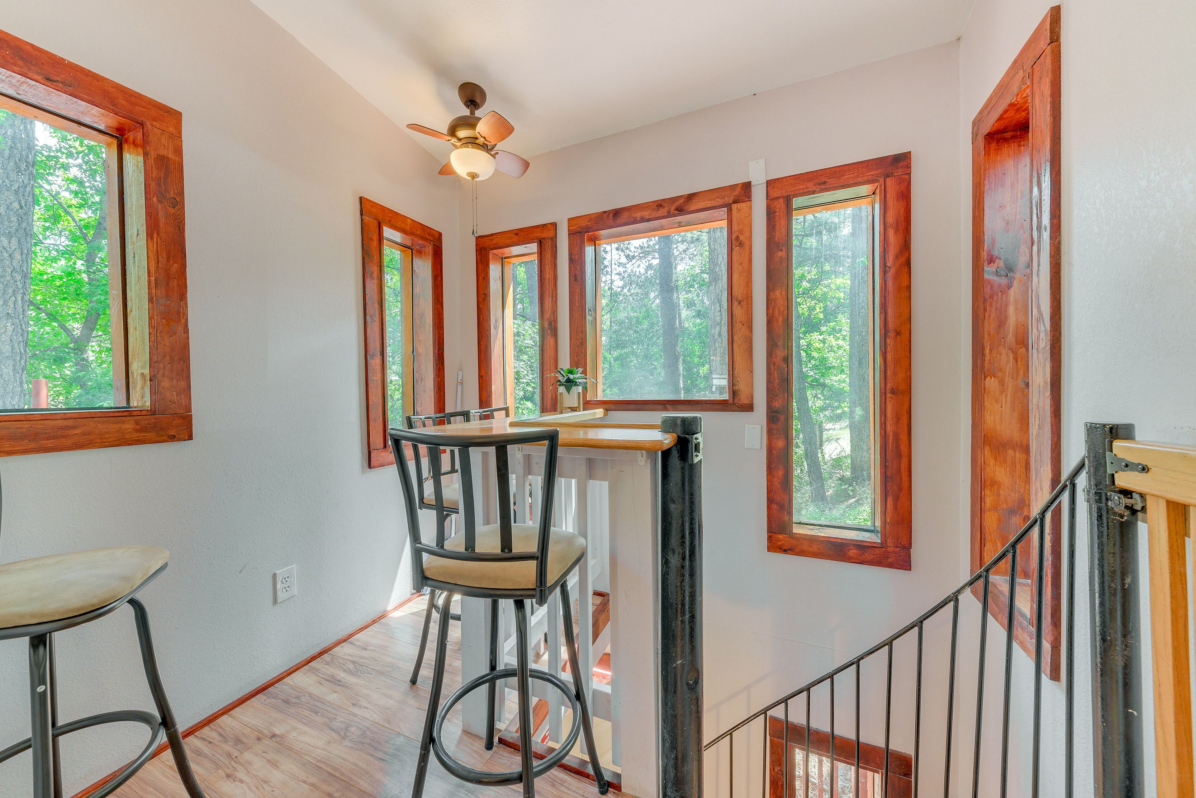A kitchen with a bar stool, wooden windows, and a ceiling fan.