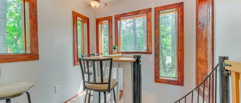 A kitchen with a bar stool, wooden windows, and a ceiling fan.