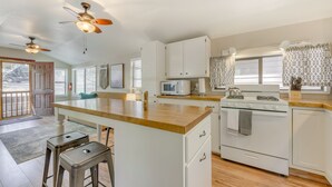 A kitchen with white cabinets, a wooden countertop, a microwave, a stove, and two bar stools. - Inn of the Mountain Goats Ruidoso Cabin w/ Deck! (Ruidoso)